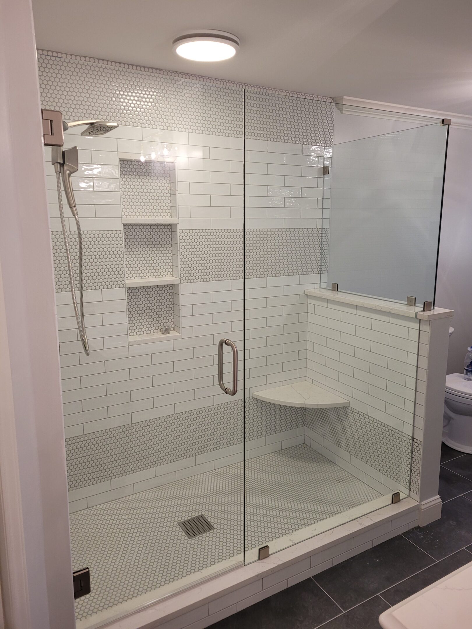 A white shower with glass doors and a bench seat.