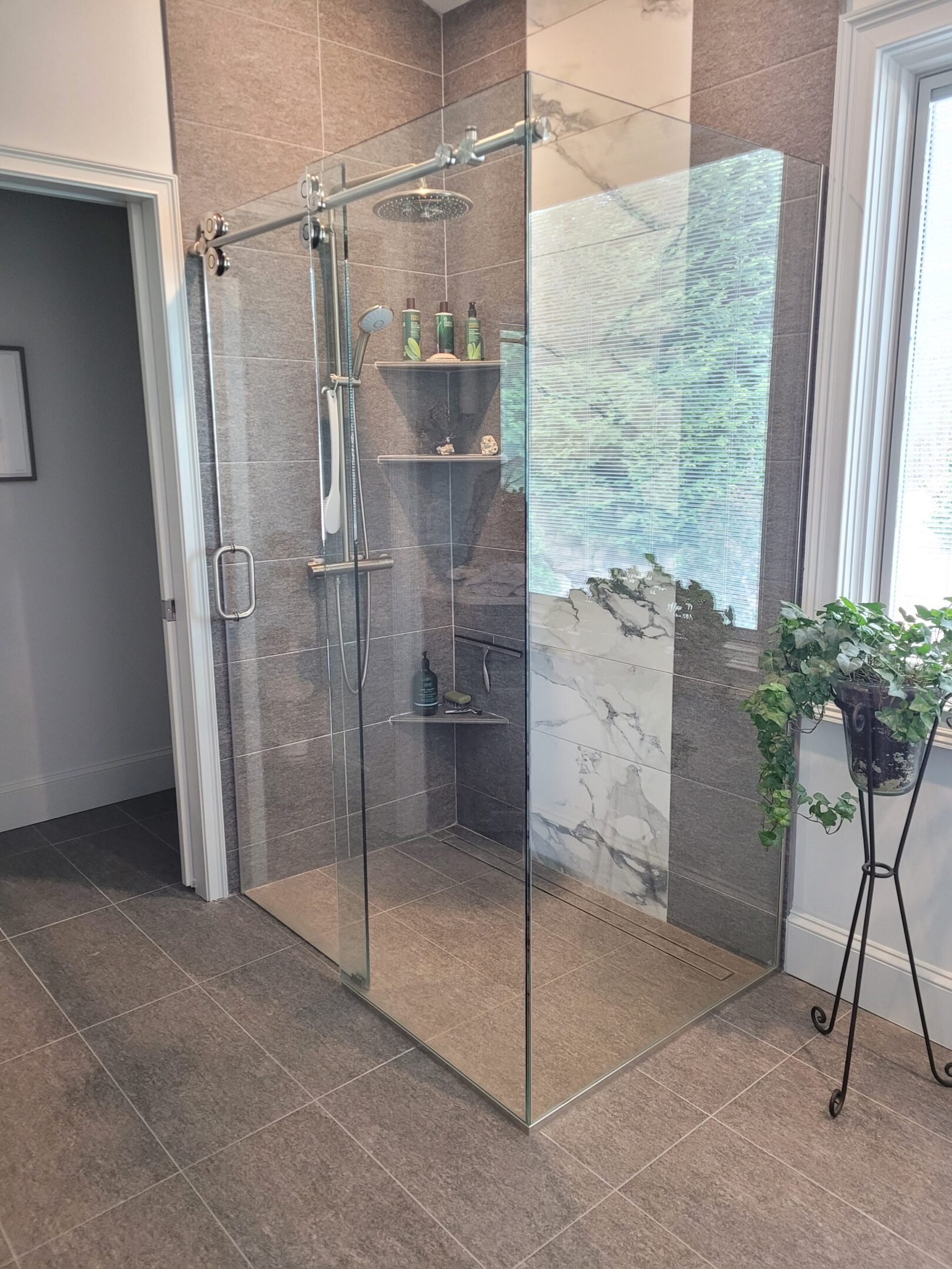 A bathroom with a glass shower door and plants.