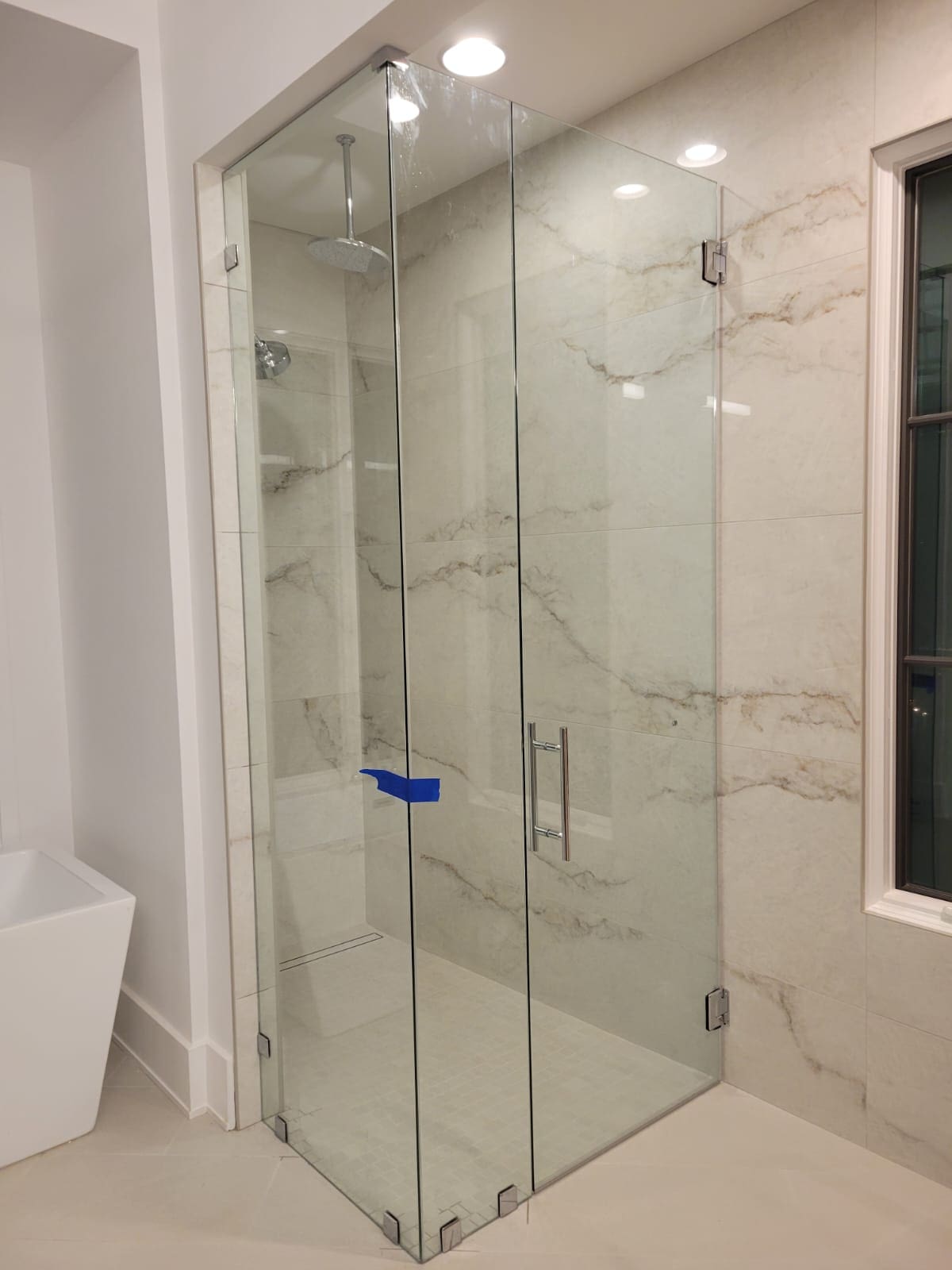 A bathroom with a glass shower door and marble walls.